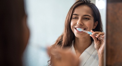 A young woman wearing a white robe and brushing her teeth to prevent gum disease