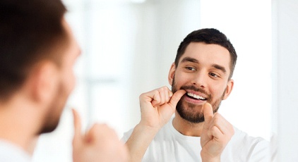 A young man using waxed dental floss to remove bacteria from teeth to prevent gum disease