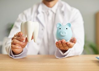 Dentist holding large model tooth in one hand and blue piggy bank in the other