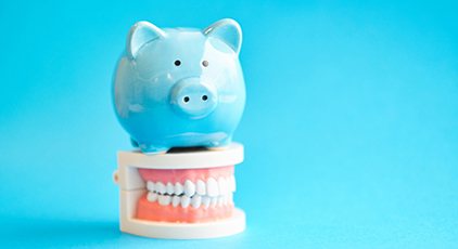 Piggy bank and model teeth symbolizing the cost of dental implants in Kernersville