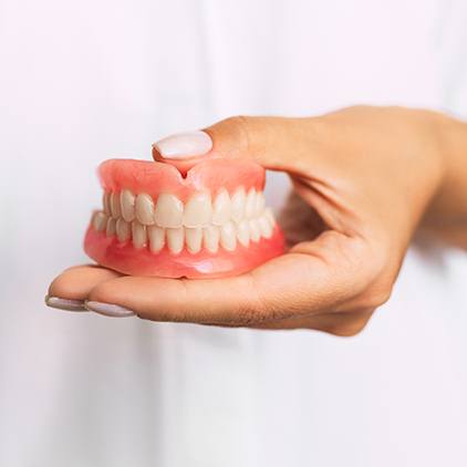 One hand holding a complete set of dentures