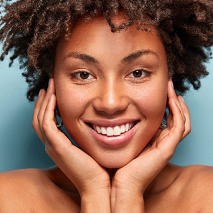 A young woman with her hands on both sides of her face smiling after learning she doesn’t have gum disease in Kernersville