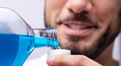 An up-close image of a man pouring mouthwash into a small cup to prevent gum disease