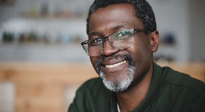 An older man wearing glasses and a polo shirt, smiling because he does not show signs of gum disease