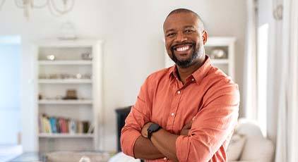 smiling man in an orange button-up shirt standing with his arms crossed