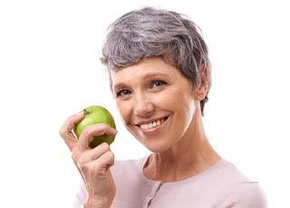 smiling woman with dental implants in Kernersville holding an apple