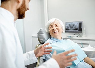 An older woman smiling as she listens to her dentist discuss dental implants