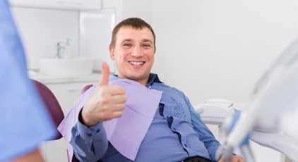 Smiling man sitting in dental chair and giving thumbs up for relaxation dentistry