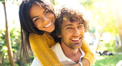 Couple smiling and hugging outside after porcelain veneer placement