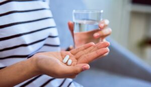 Person holding 2 pills in one hand and a glass of water in the other.